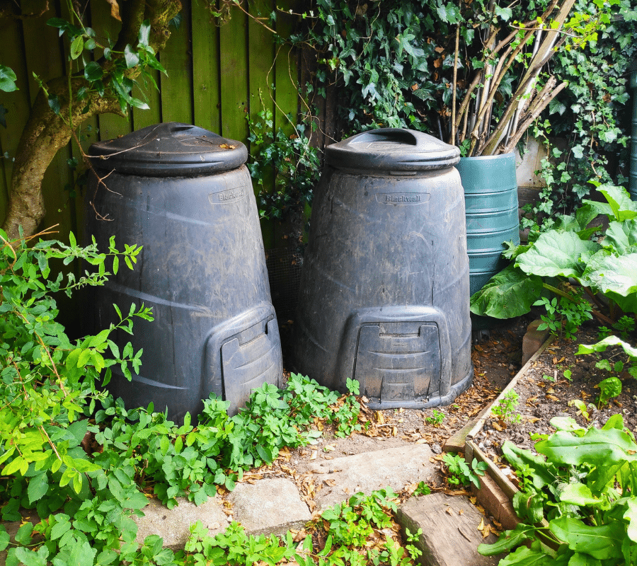 two black compost bins in a garden